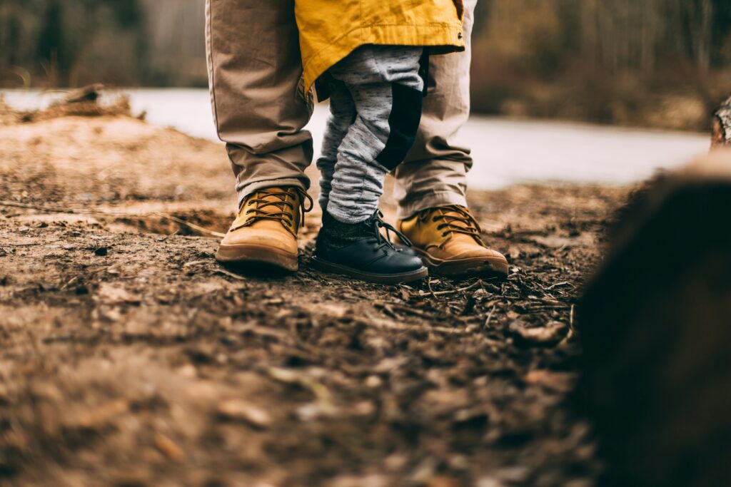 Die Balance von beruflicher Vision und Elternrolle - Beitragbild - Schuhe von Vater und Kind auf dem Waldboden